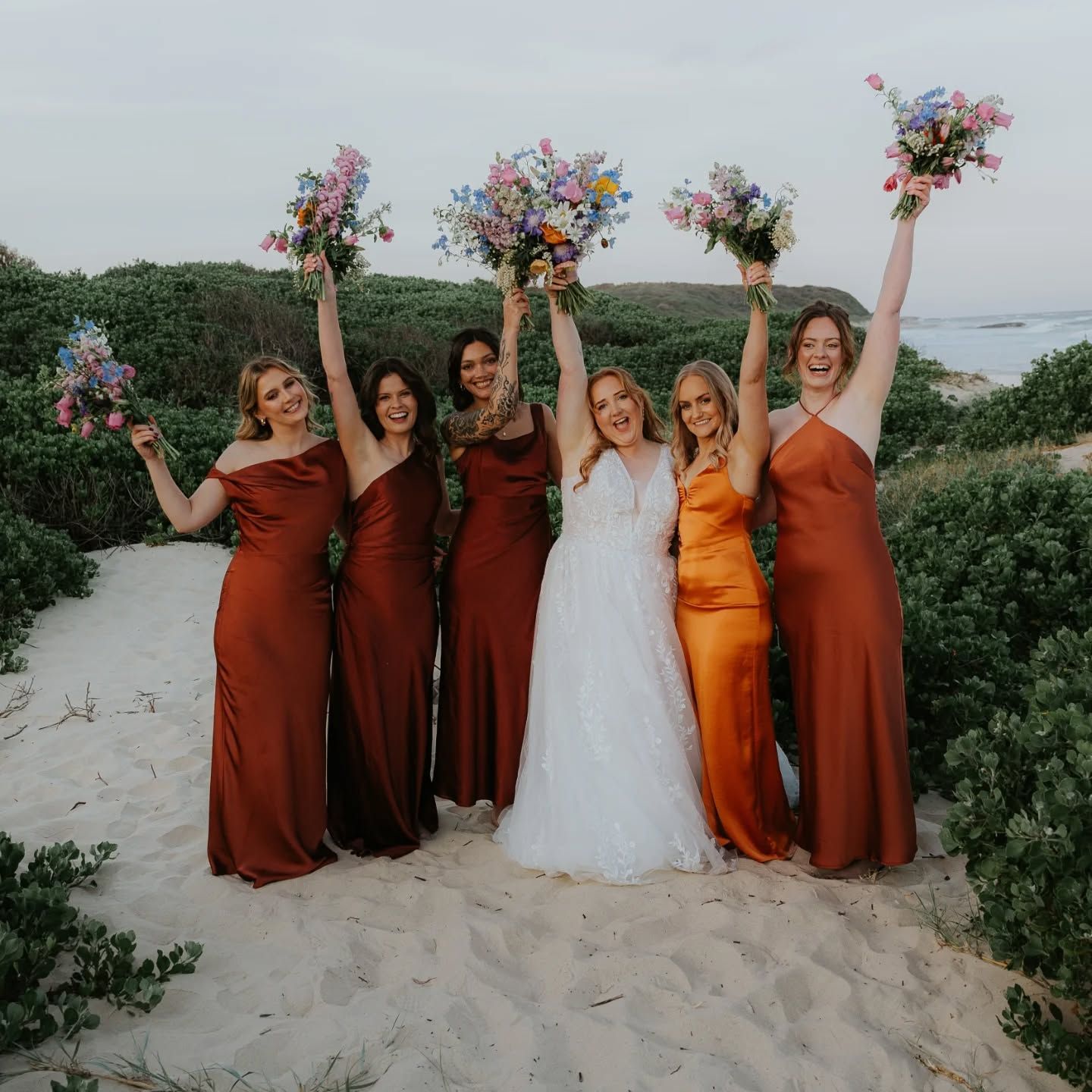 Bridesmaids on a beach raising colourful wildflower bouquets