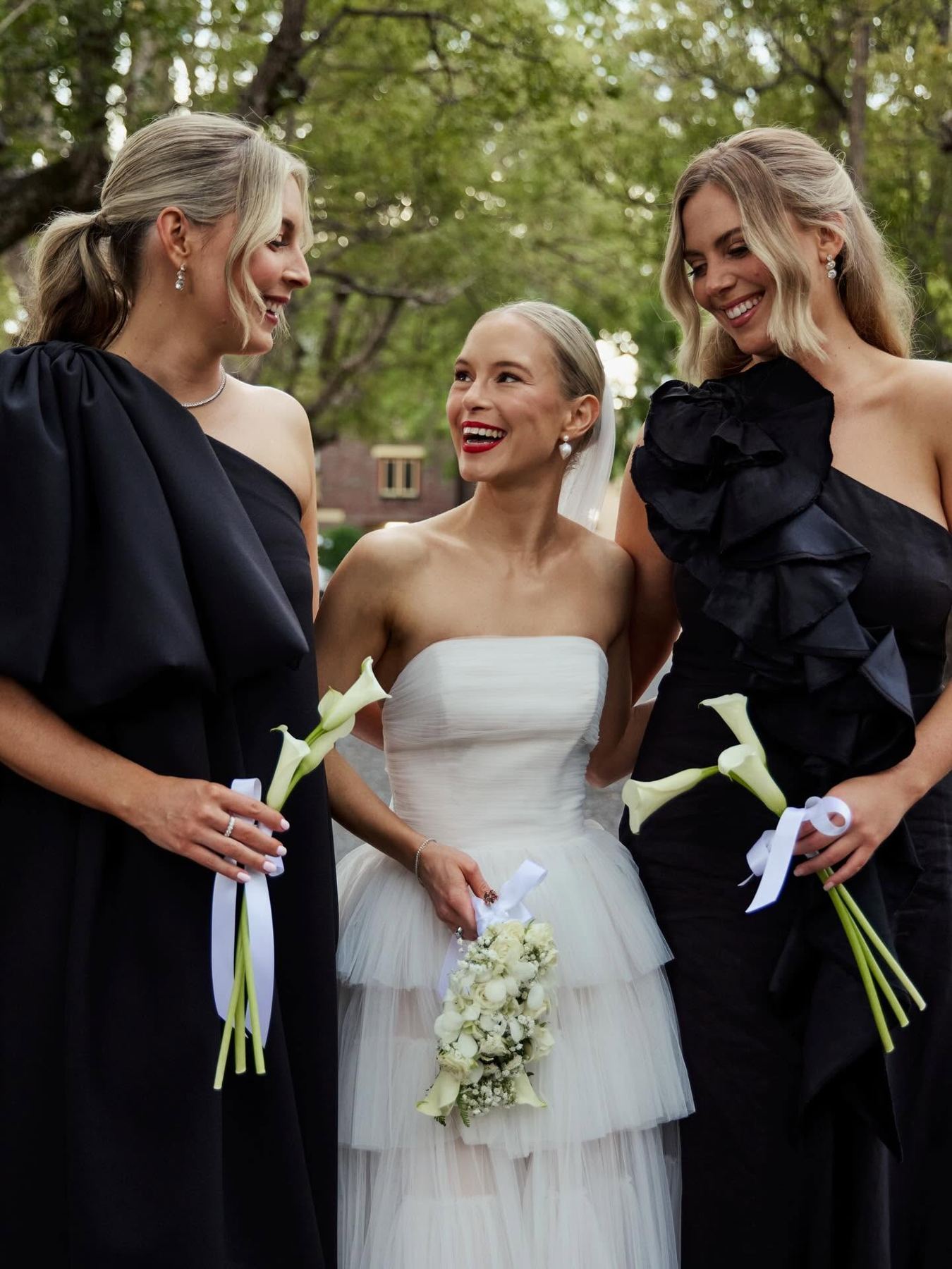 Bride with two bridesmaids in black dresses holding calla lily bouquets