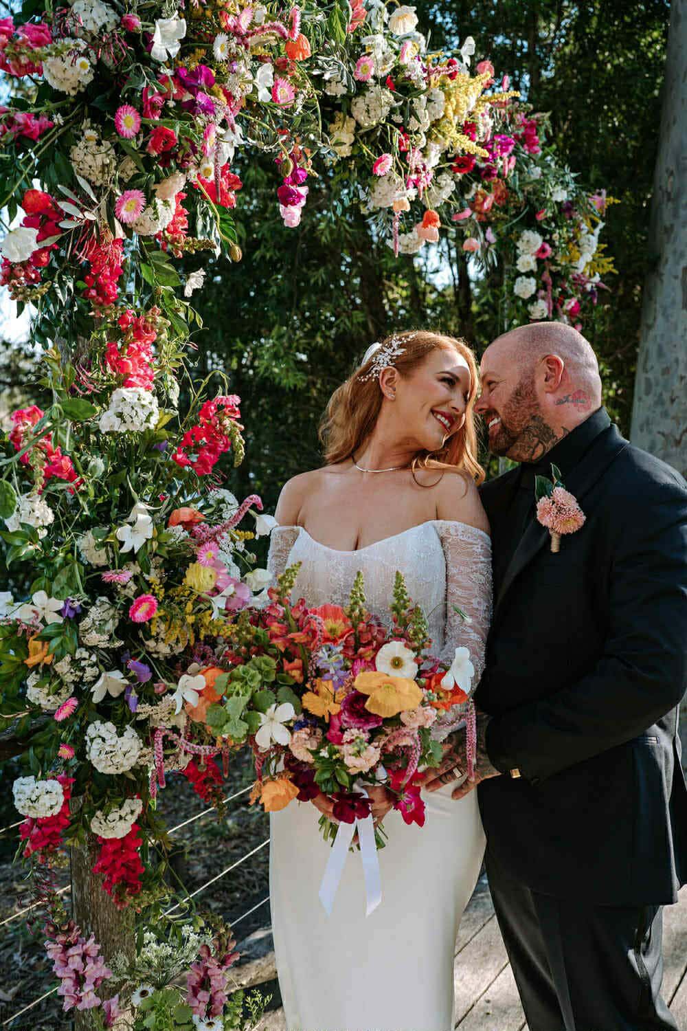 Bride and groom embracing under a colourful floral arch