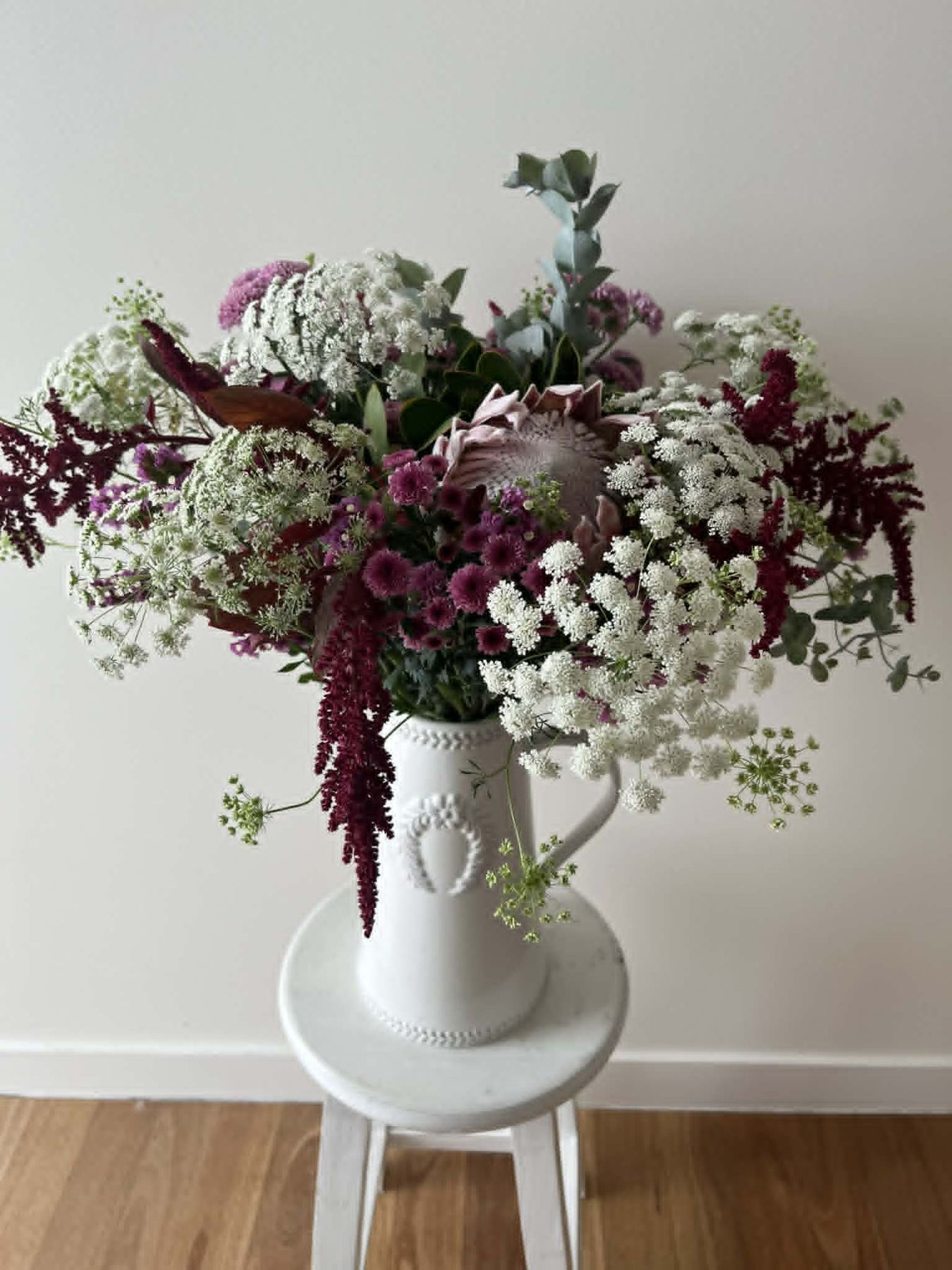 White jug arrangement with white and burgundy seasonal flowers