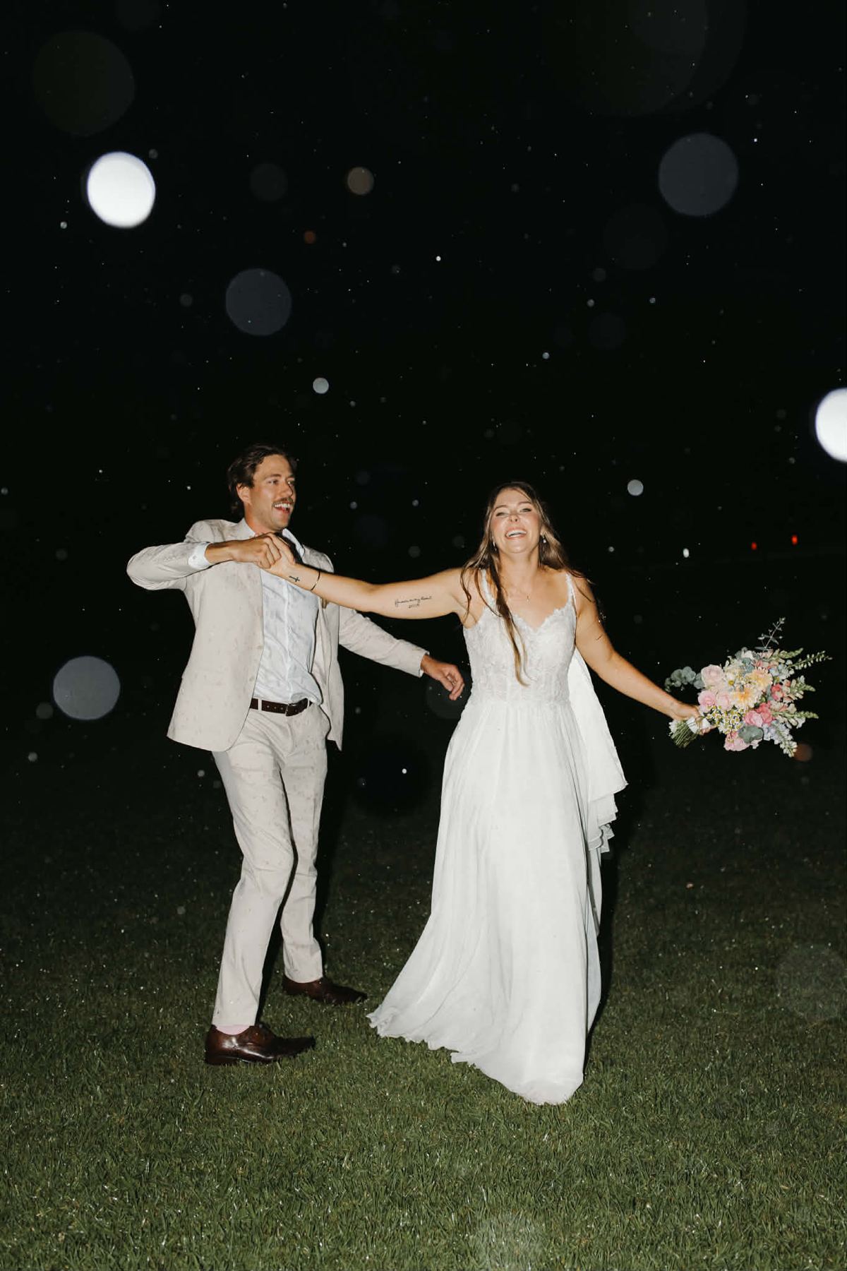 Bride and groom laughing and dancing in the rain at night