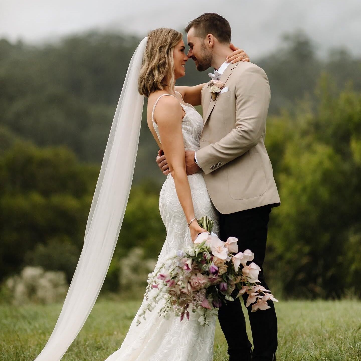 Bride and groom embracing, holding a pastel wedding bouquet