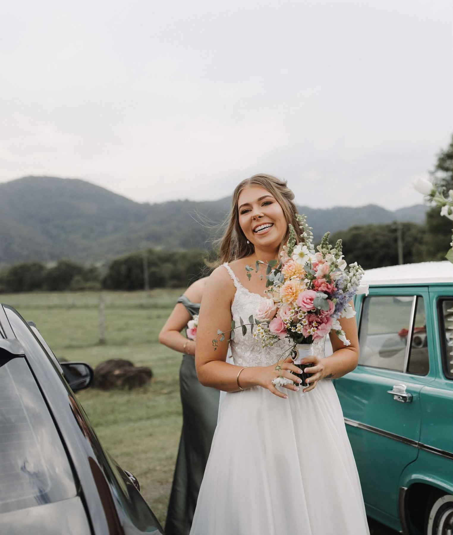 Bride smiling beside a vintage car holding a pastel bouquet
